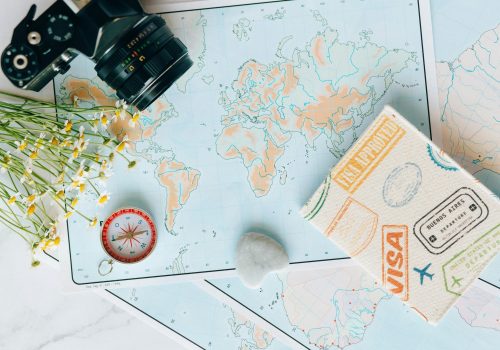 Flat lay of travel essentials: maps, camera, compass, and travel journal for planning adventures.